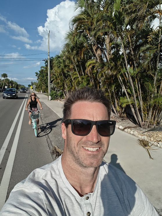 Cyclists enjoying a sunny afternoon ride on a paved path lined with lush palm trees under a bright blue sky.